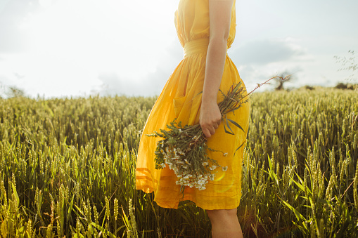 Photo of a young woman standing alone on a grass field holding a bouquet of wild flowers