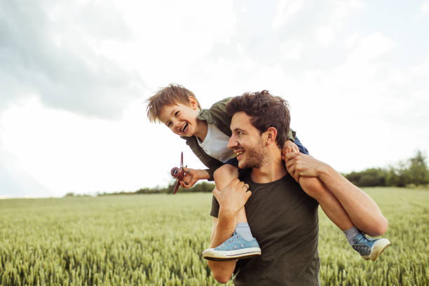 Future airplane pilot Photo of a cheerful little boy, being supported to be a pilot, by his father who is holding him on shoulders on shoulders stock pictures, royalty-free photos & images