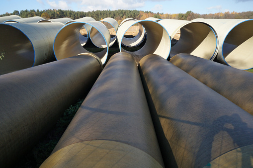 Large sewer pipes  lie on sand and dirt  in a autumn forest  construction site.  Sunny October day outoor industrial shots