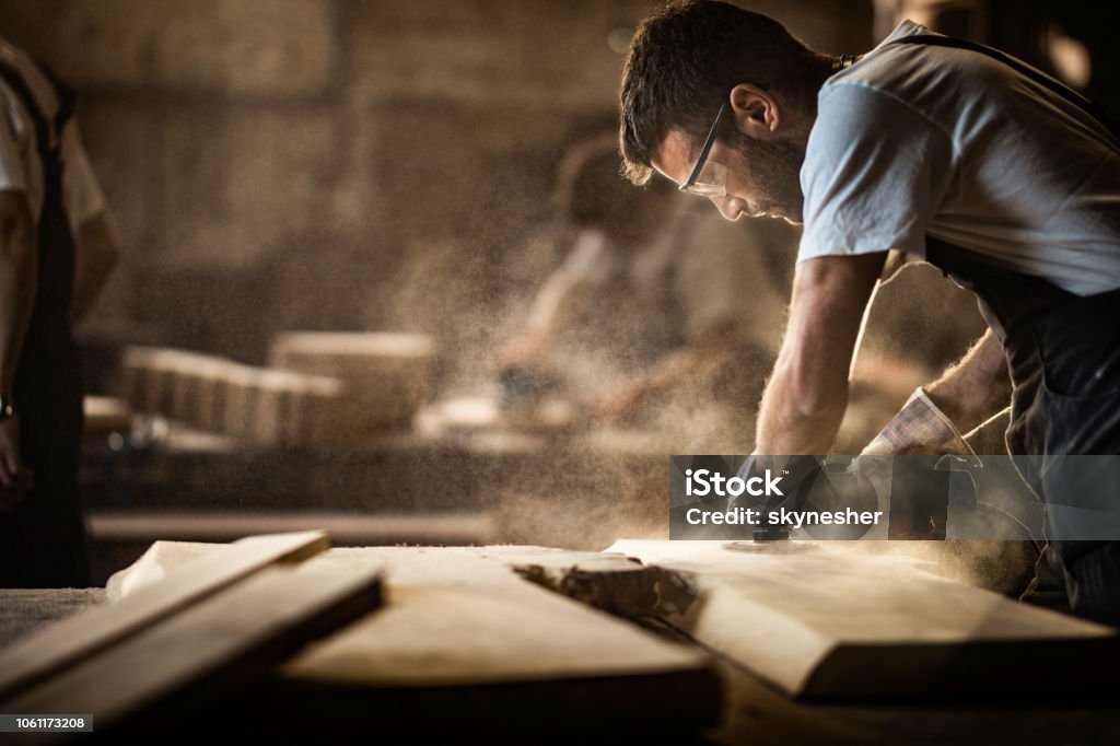 Junge Tischler mit Sander während der Arbeit an einem Stück Holz. - Lizenzfrei Schreiner Stock-Foto
