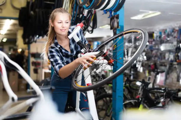 Young woman master is fixing wheel of bicycle in workshop