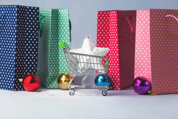 Christmas shopping concept. Shopping cart, colors bags, christmas multi-colored balls, on a light background