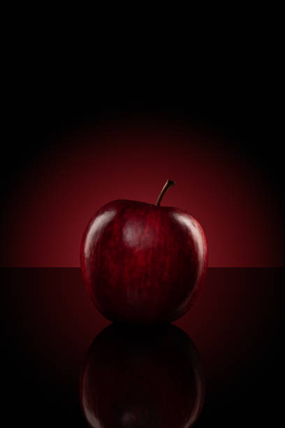 istock An apple isolated on reflective black board with red glowing light background 1061190004
