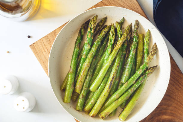 vista dall'alto sugli asparagi arrostiti in una padella bianca su un tavolo da cucina. stile moderno, cibo vegetariano. - asparagus foto e immagini stock