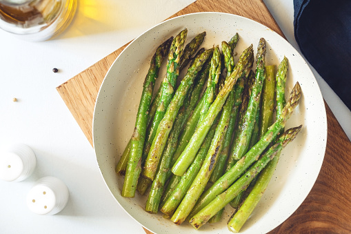 Top view on roasted asparagus in a white pan on a kitchen table. Modern style, vegetarian food.