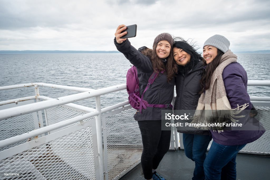 Winter Travel on Ferry, Mother and Teen Daughters Taking Selfie Asian mother and Eurasian teen daughters on deck of ferry between Vancouver and Nanaimo, British Columbia, Canada. Winter Stock Photo