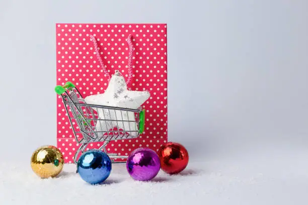Christmas shopping concept banner. Shopping cart, red bag, christmas multi-colored balls and star, on light background. Copy space
