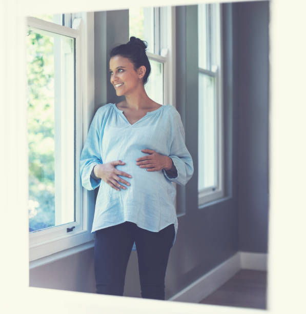 istock Smiling pregnant woman looking through window 1061195540