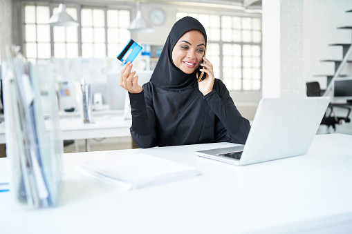 Sonriendo a empresaria árabe hablando por teléfono y que tarjeta de crédito photo