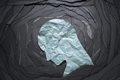 Negative emotion image. Person head shaped paper on black torn paper background.
