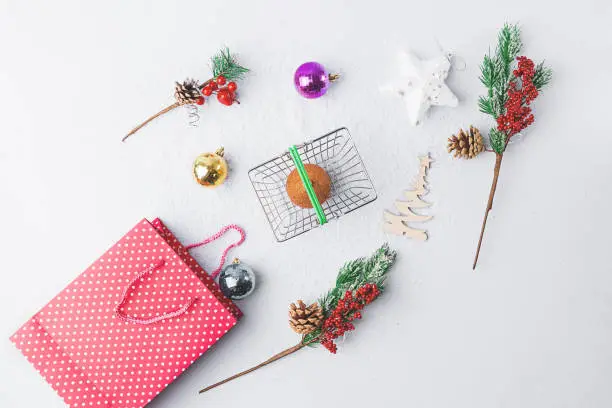 Christmas shopping gift concept composition. Shopping basket, christmas multi-colored balls, red bag and branches trees, top view. Flat lay
