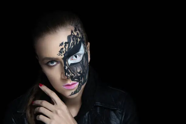 Creative makeup for crazy Halloween party, black lines paint streaks. Big white eye, half face evening makeup, pink glamour lipstick. Original idea for holiday. Professional concept. Young sexy girl