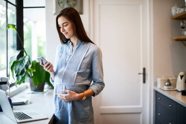 młoda kobieta w ciąży za pomocą telefonu komórkowego w kuchni - window human pregnancy home interior women zdjęcia i obrazy z banku zdjęć