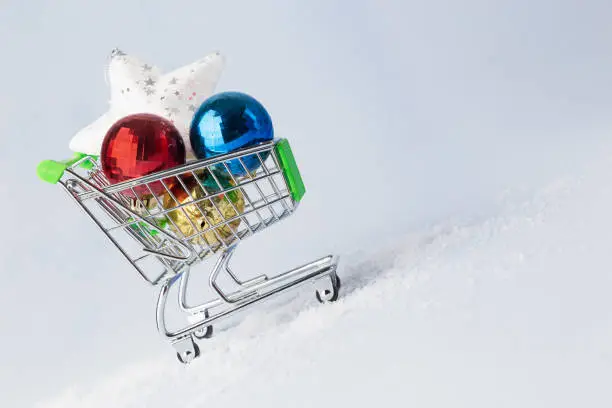 Christmas shopping minimal concept. Shopping cart, christmas multi-colored balls and star, on light background. Copy space