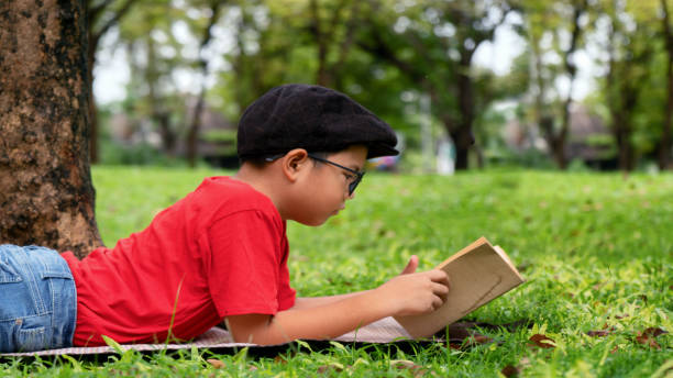 istock Asian boy in red shirt having fun reading book under tree in park 1061216962