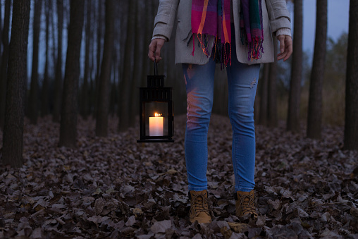 Woman with candle lantern walking in the woods at autumn night.