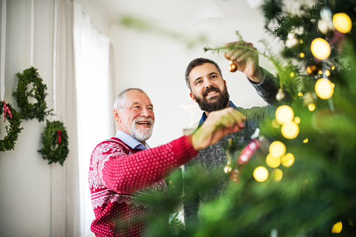 A senior father and adult son decorating a Christmas tree.