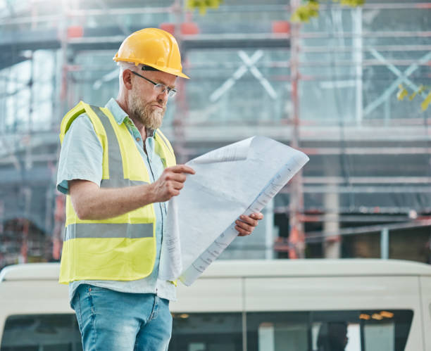 Mature building professional studying plans on construction site seriously