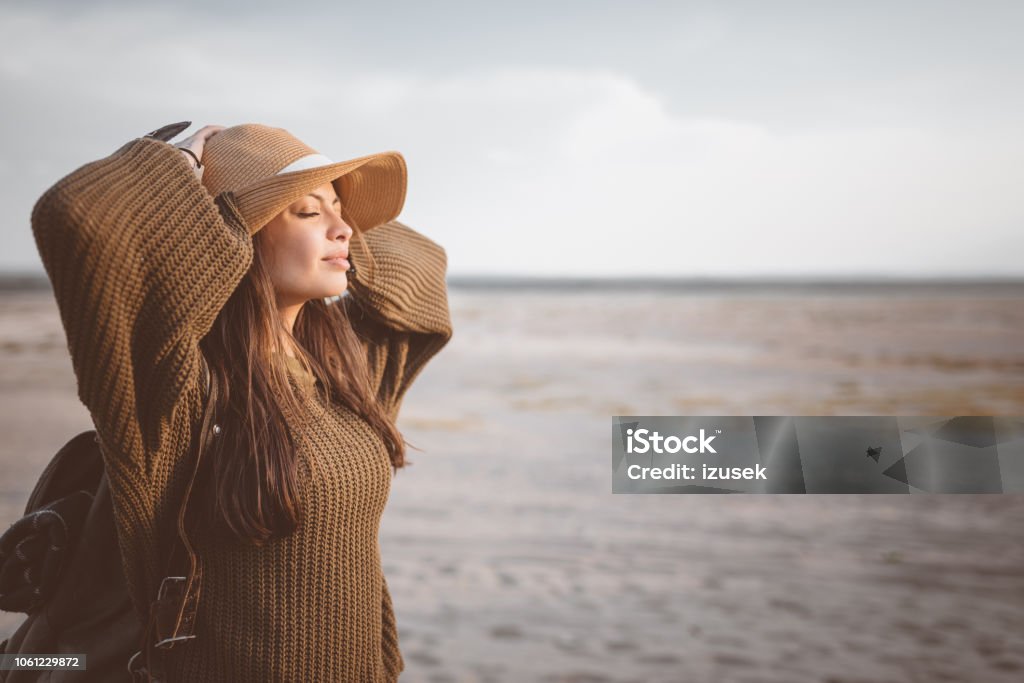 Outdoor shot of young woman resting on the desert Outdoor shot of beautiful young woman standing against desert, holding backpack and enjoying sunset. Independence - Concept Stock Photo