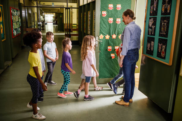 Happy female teacher welcoming elementary students in the classroom.