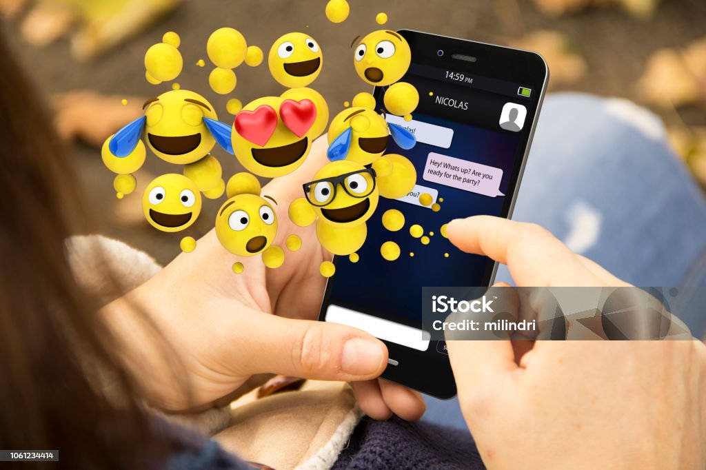 woman sending emoticons with the phone at the park mobile design concept: woman holding a 3d generated smartphone and sending emoticons. Graphics on screen are made up. Emoticon Stock Photo