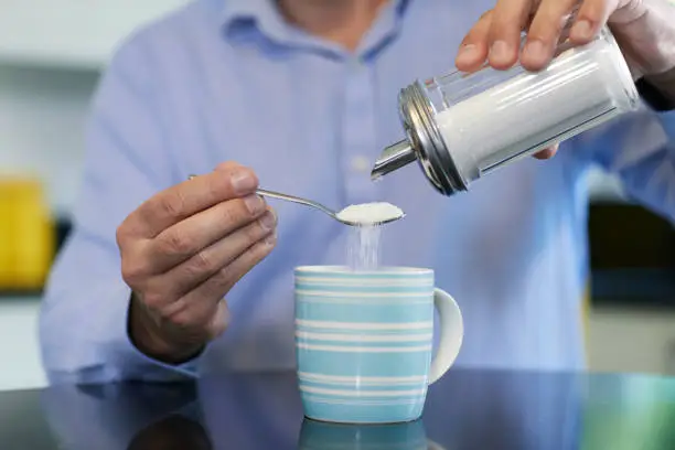 Photo of Close Up Of Mature Man Adding Sugar To Hot Drink At Home