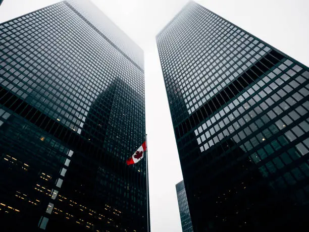 Two office buildings dwarf a flag pole sporting the Canada flag, as seen from the center of a courtyard in downtown Toronto.