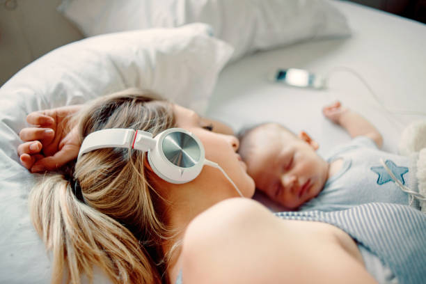 音楽を聴くと、彼女の赤ちゃんと昼寝の母 - parent mother music listening ストックフォトと画像