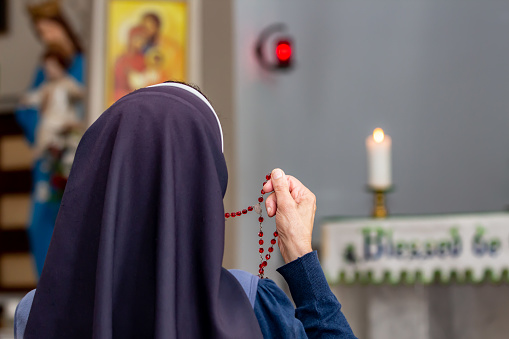 View from back of a religious sister holding rosary and praying.