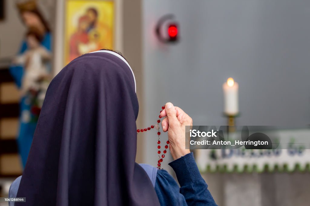 View from back of a religious sister holding rosary and praying. View from back of a religious sister holding rosary and praying at altar in church chapel. Nun Stock Photo