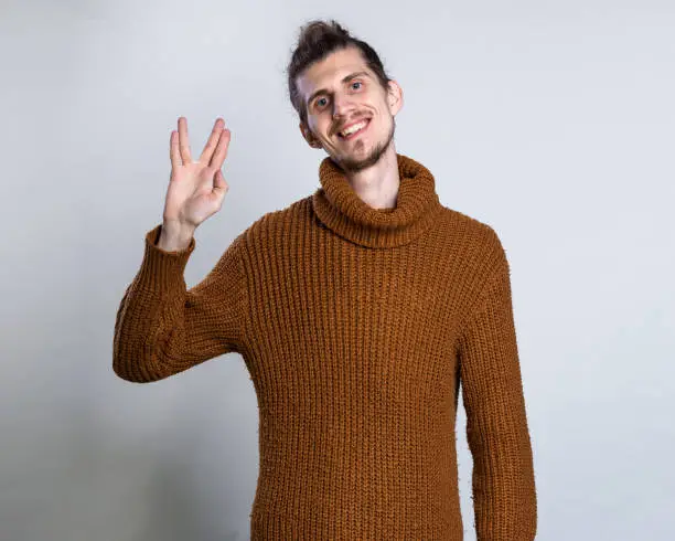 Geek saluting concept. Men in warm knitted sweater welcomes fans of fiction films Vulcan greeting on grey background copy space