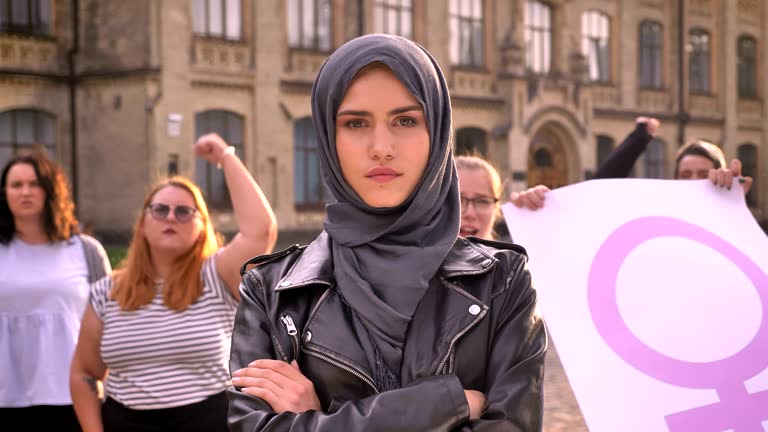 Group of various caucasian feminists with cute girl in hijab in center attracting attention with pink flag and voting outdoor