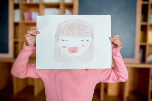 chica joven sosteniendo un autorretrato dibujado delante de su cara - autorretrato fotografías e imágenes de stock