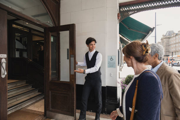 We Hope You Enjoy Your Stay Mature couple are arriving at a hotel and a doorman is welcoming them in. door attendant photos stock pictures, royalty-free photos & images