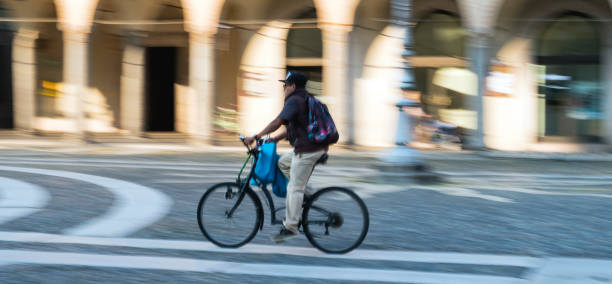 Vigevano, Italy - October 12, 2018: one man of asian ethnicity running with a bike in the reinassance square of Vigevano (Lombardy, Nortehrn Italy), named Piazza Ducale; built at the end of XVII Century. Photo taken in a public place.
