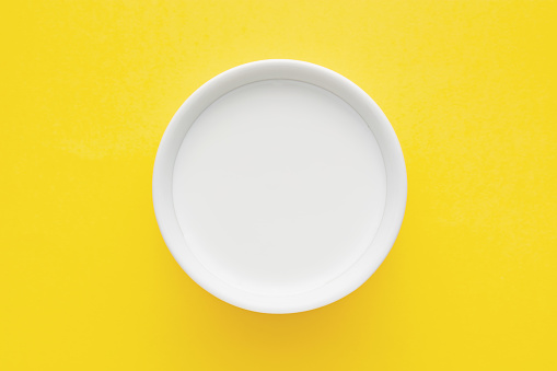 Top down minimalist view of a milk in a white bowl on tellow background