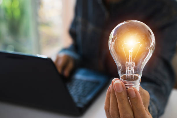 Business woman holding light bulb on the desk in office and using  computer in  financial,accounting,energy,idea concept. Business woman holding light bulb on the desk in office and using  computer in  financial,accounting,energy,idea concept. resourceful stock pictures, royalty-free photos & images