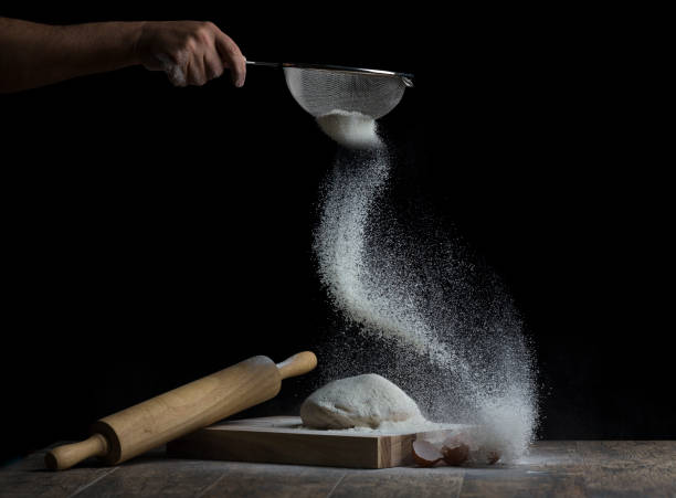 Flour is sprinkled over a ball of dough on a wooden board with roller and eggs stock photo