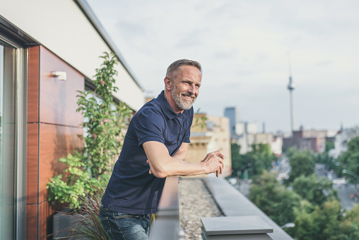 relaxed bearded midaged man standing on balcony in Berlin  summer