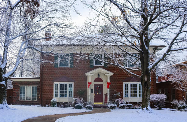 beautiful brick house with bay windows with christmas tree showing through and decorated pillars and sled on porch in snow framed by winter trees - window snow christmas decoration imagens e fotografias de stock