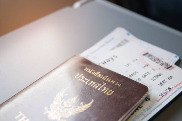 istock Airplane tray table on seat back inside cabin; Thai passport, ticket and immigration bureau card with sun shining through the window. 1061381558
