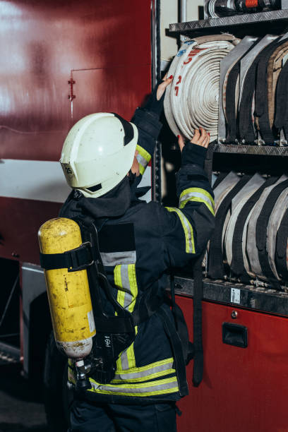 istock partial view of female firefighter with fire extinguisher on back putting water hose into truck at fire department 1061386086