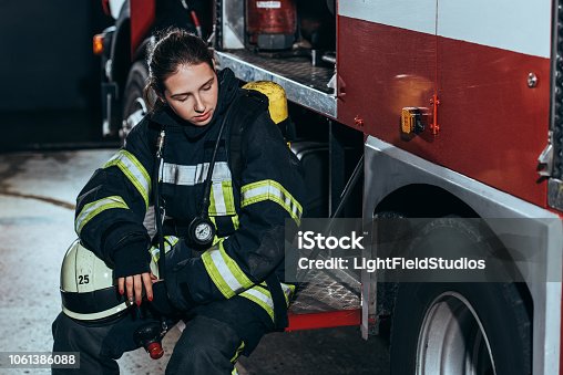 istock tired female firefighter in uniform with helmet sitting on truck at fire station 1061386088