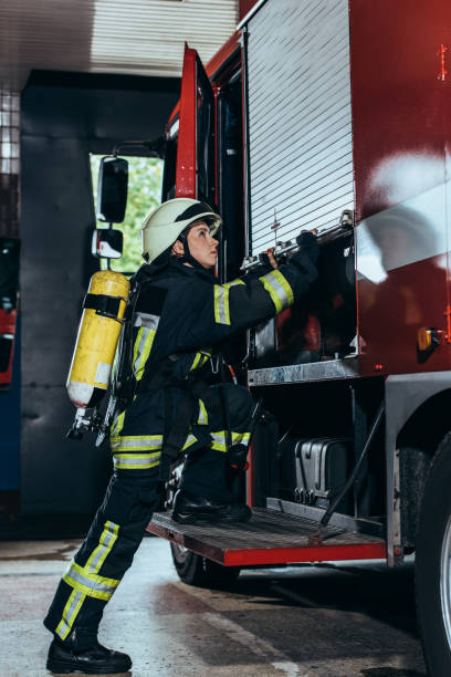 istock side view of female firefighter with fire extinguisher on back closing truck at fire department 1061386232