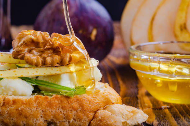 bruschetta with cheese, fruit and nuts is drizzled with honey, on a wooden table. Macro. bruschetta with cheese, fruit and nuts is drizzled with honey, on a wooden table. Macro. тост stock pictures, royalty-free photos & images