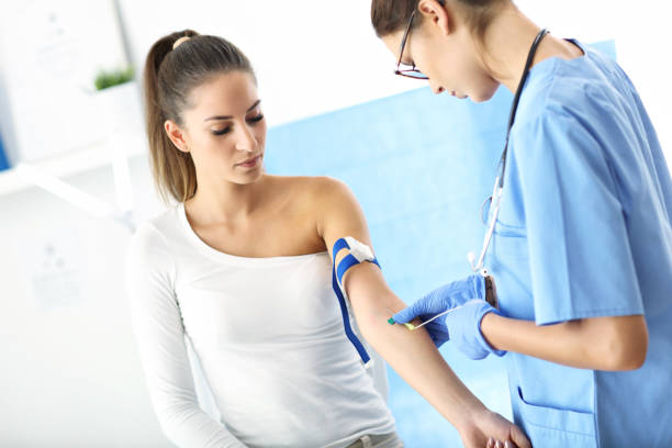 Adult woman having blood collection visit at female doctor's office stock photo