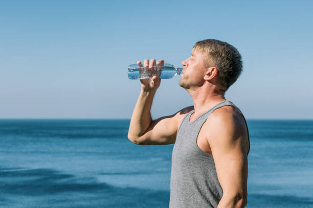 A man pours water on his face from a plastic bottle on the ocean