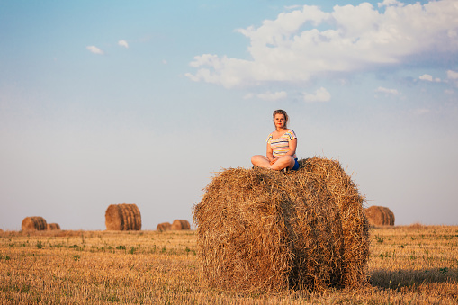 Beautiful Plus Size Young Woman In Shirt Sit On Hay Bales In Summer Field Meadow At Blue Sly Background