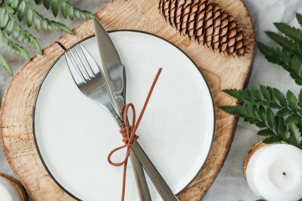 istock Festive table setting among winter decorations and white candles. Ceramic plate, fork and knife on a wooden decorative tray. The concept of a Christmas or Thanksgiving dinner. 1061439228