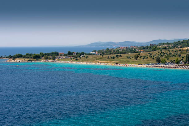 The coastline of Sithonia, Greece, in good sunny weather. A strip of sandy beaches and blue sea water against the background of distant mountains and hills.
